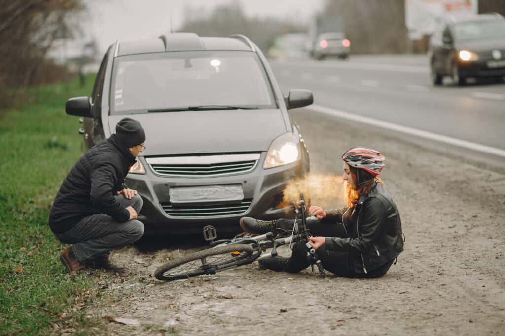 A bicyclist sitting on the road in front of a car and its driver after a crash
