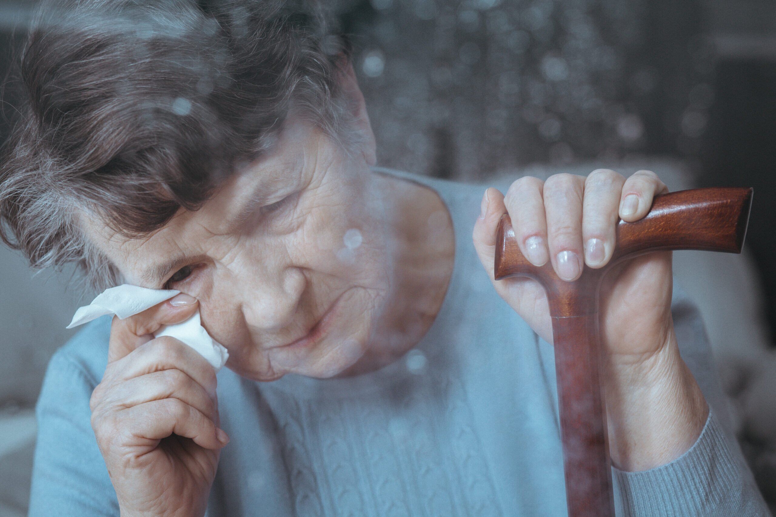 Sad senior woman crying, holding walking stick and tissue.